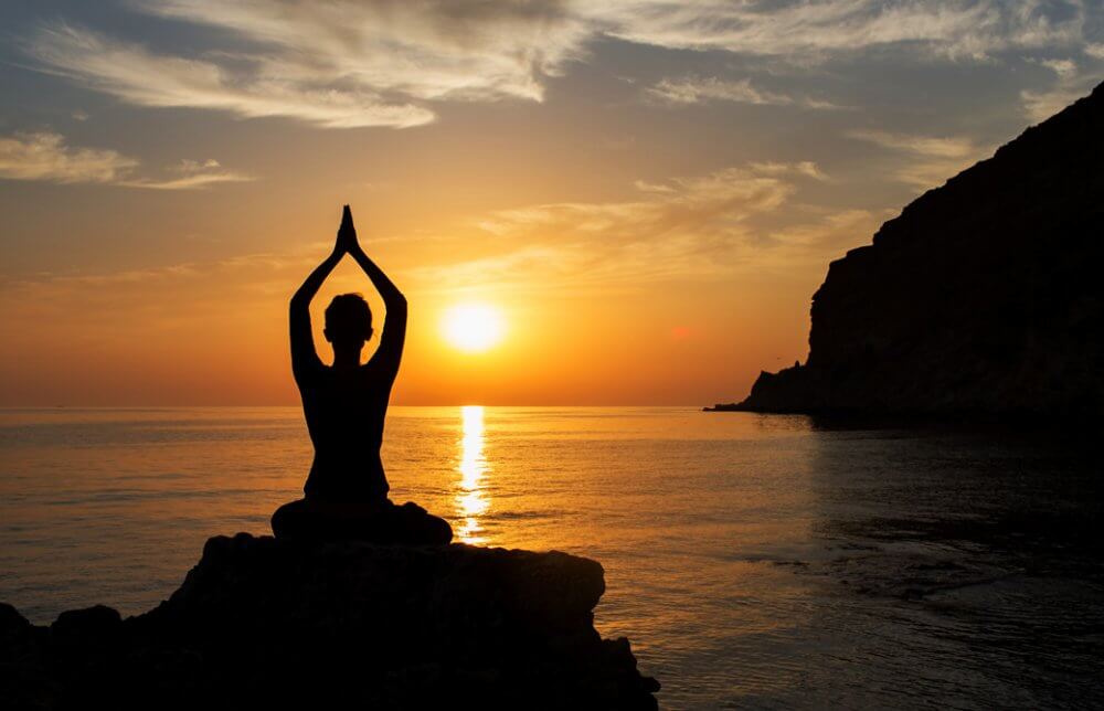 インドのゴアで夕日に向かって瞑想をしている女性のシルエット