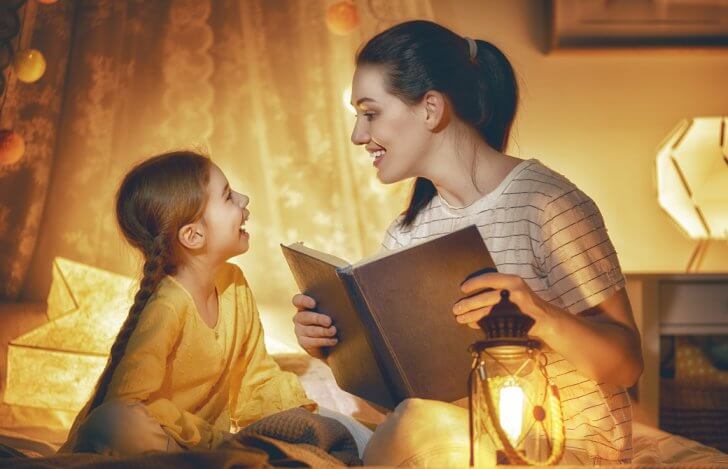 母親が幼い娘に微笑み合いながらベッドで絵本を読んであげている