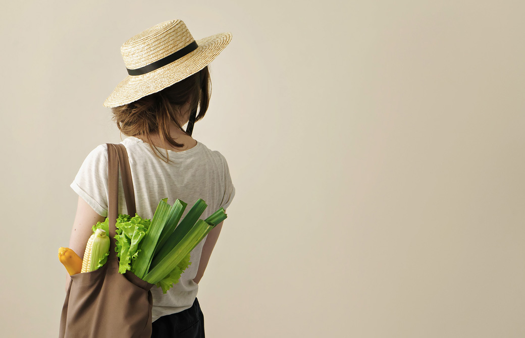 エコバッグに野菜を入れて肩にかけている帽子をかぶった女性の後ろ姿