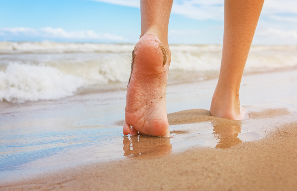 裸足でビーチを歩いている女性の足もと