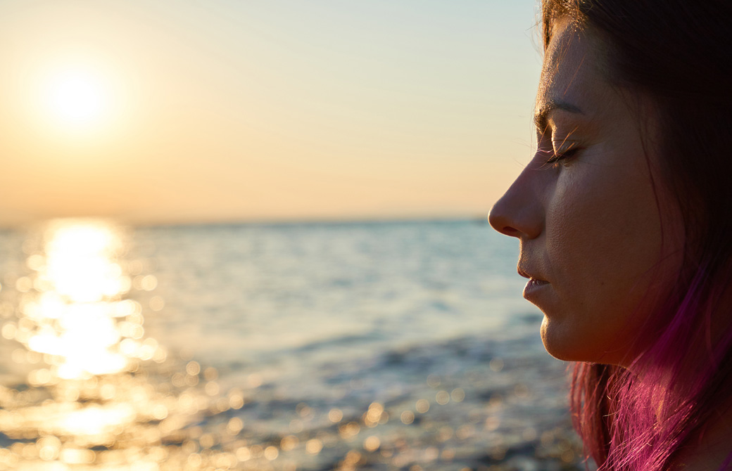 夕陽の海辺で目を閉じている女性の横顔