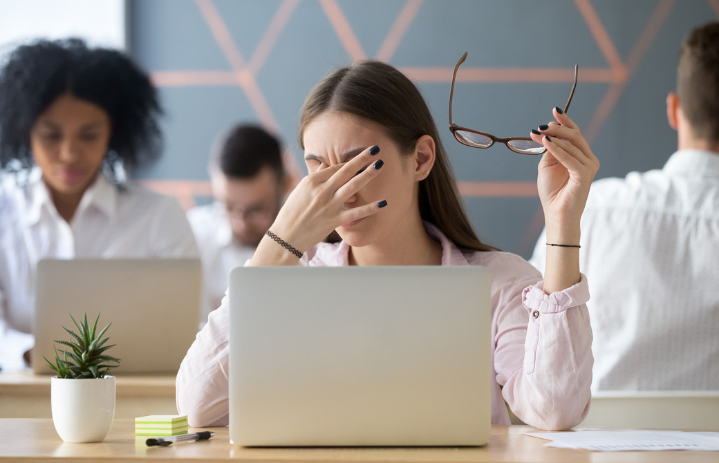オフィスのパソコンデスクで眼鏡をはずして眼の疲れをほどこうとしている女性