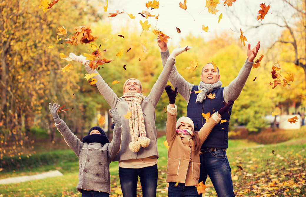 秋の公園で枯れ葉を撒いて楽しむ4人家族