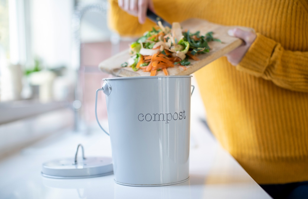 コンポストの入れ物に野菜の切れ端などを入れている女性の手元
