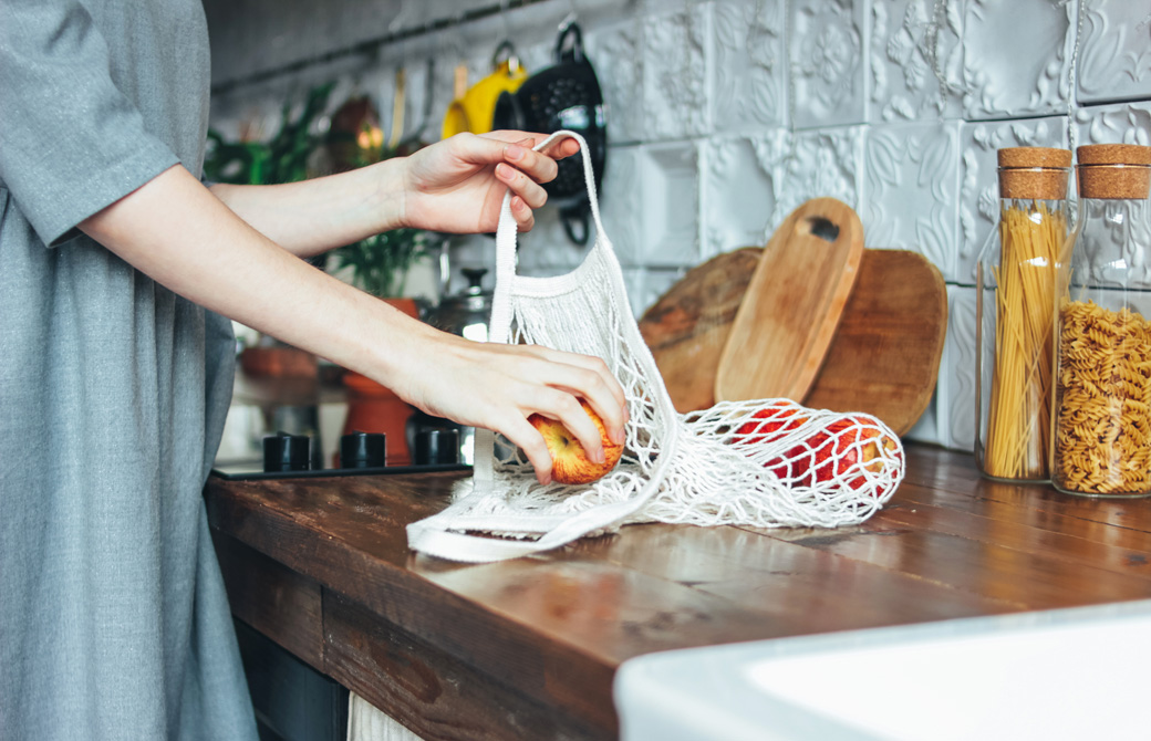 調理台の上でエコバッグからリンゴを取り出している女性の腕