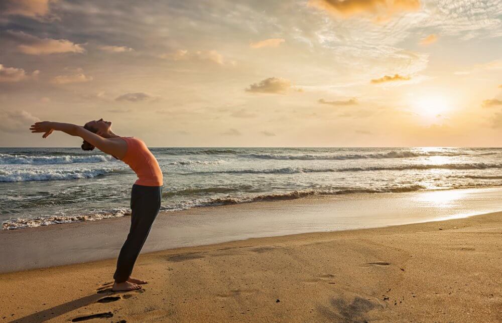 浜辺で朝日に向かって太陽礼拝をしている女性