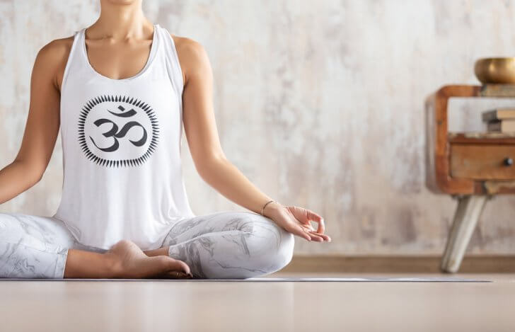 オームのシンボルが描かれたタンクトップを着て瞑想する女性