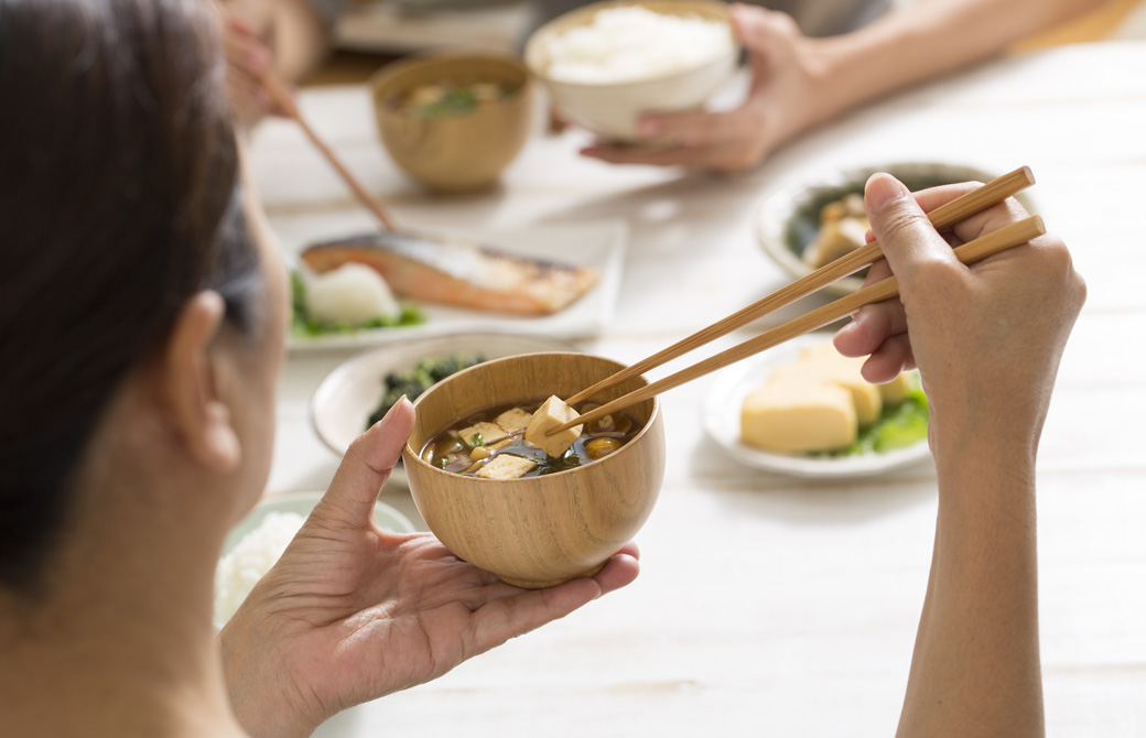 豆腐のみそ汁を飲もうとしている女性と朝食の風景