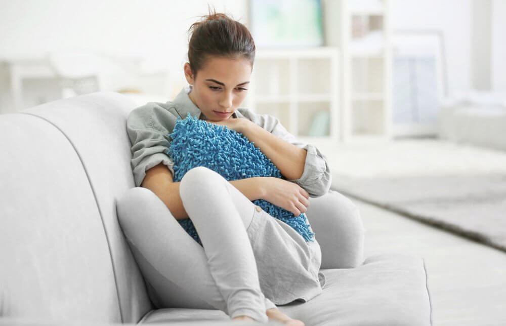 ソファで青いクッションを抱いてうつむいている女性