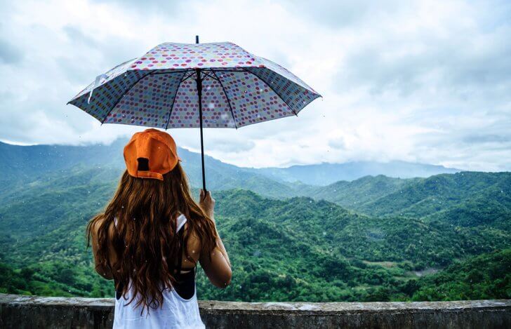 雨の中を美しい山並みに向かって傘をさしている女性の後ろ姿