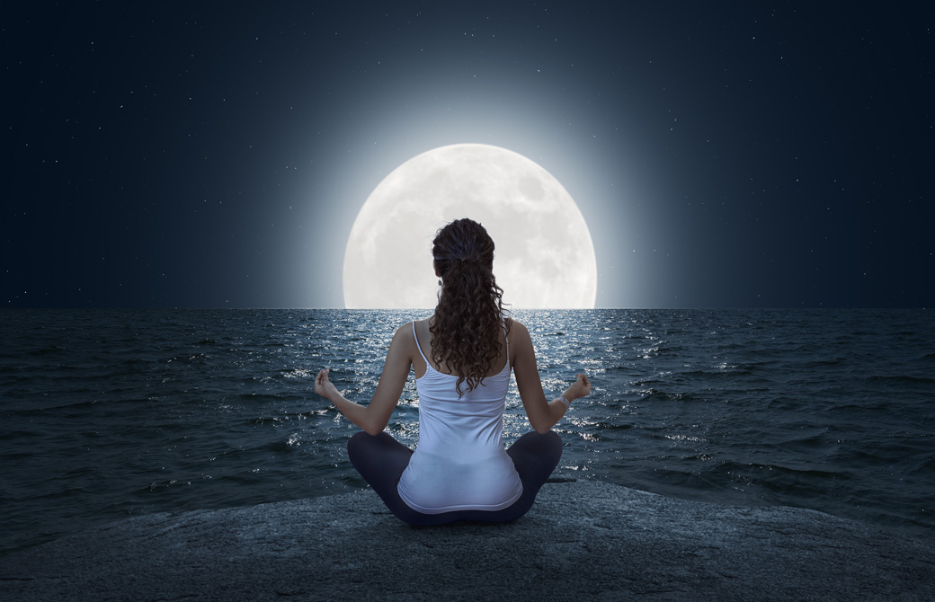 海辺で満月に向かって瞑想をしている女性の後ろ姿