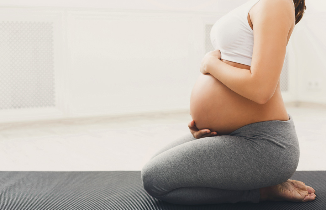 お腹の大きい妊婦がヨガマットに正座の姿勢で座っている横向きの写真