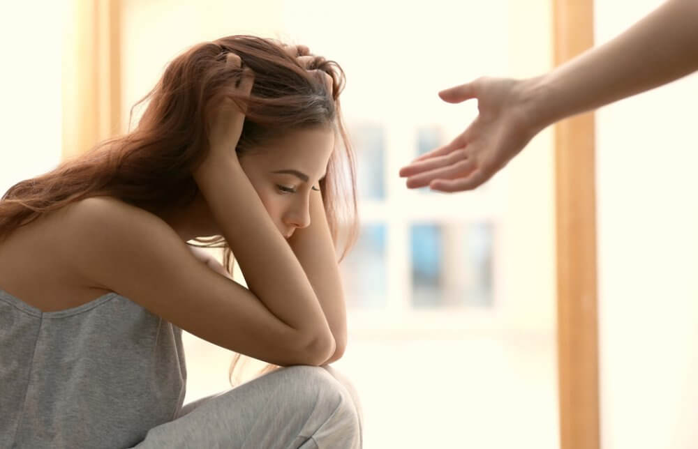頭を抱えて悩んでいる様子の女性と誰かが彼女に手を差し伸べている