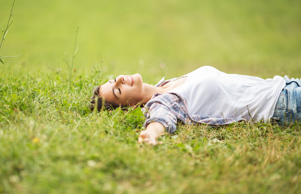 芝生で仰向けで気持ち良さそうに目を閉じ微笑んでいる女性