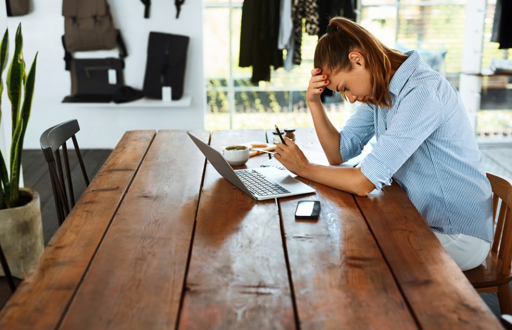 テーブルの上のPCを前に頭をかかえて悩んでいる女性