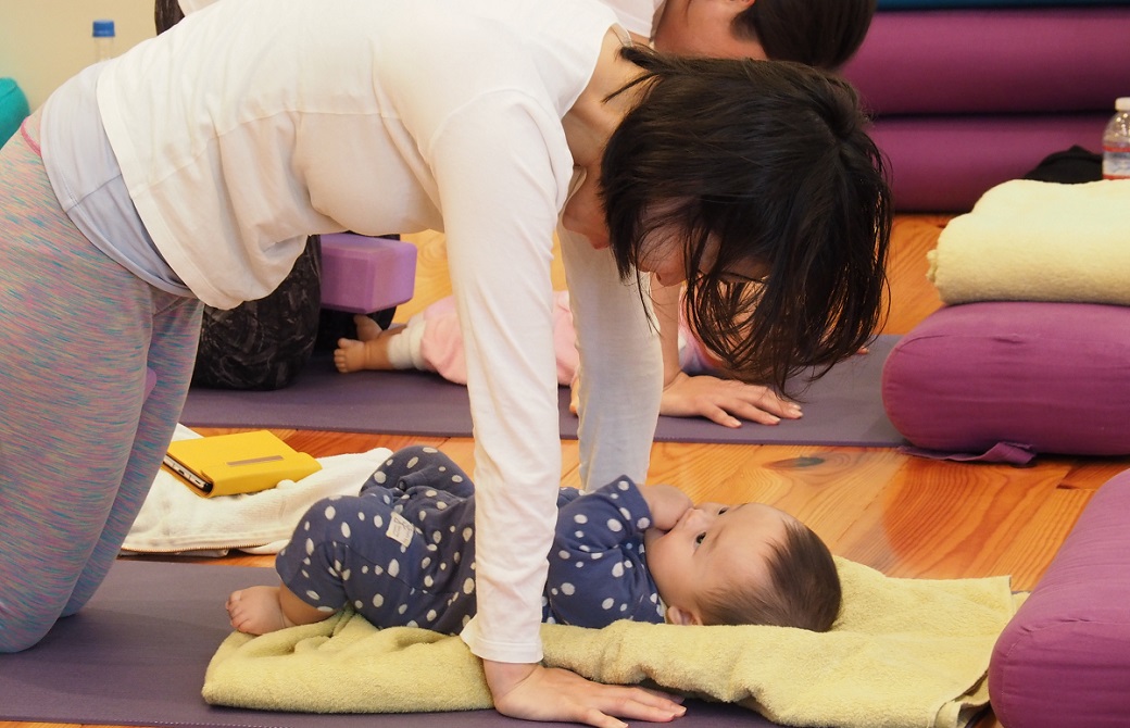 赤ちゃんをブランケットの上に寝かせて四つん這いで見つめるお母さん:産後ヨガクラス