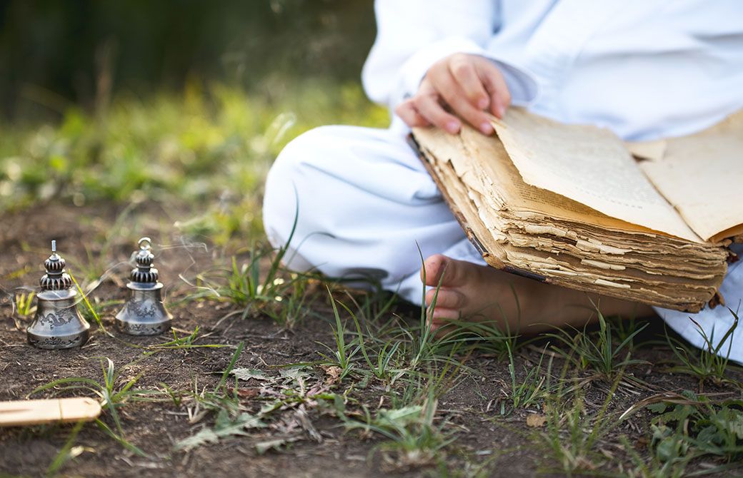 地面の上で白い服を着た男性が古書を読んでいる様子