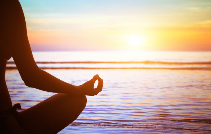 ビーチで座りながら瞑想をしている人の影が夕暮れの太陽に照らされている
