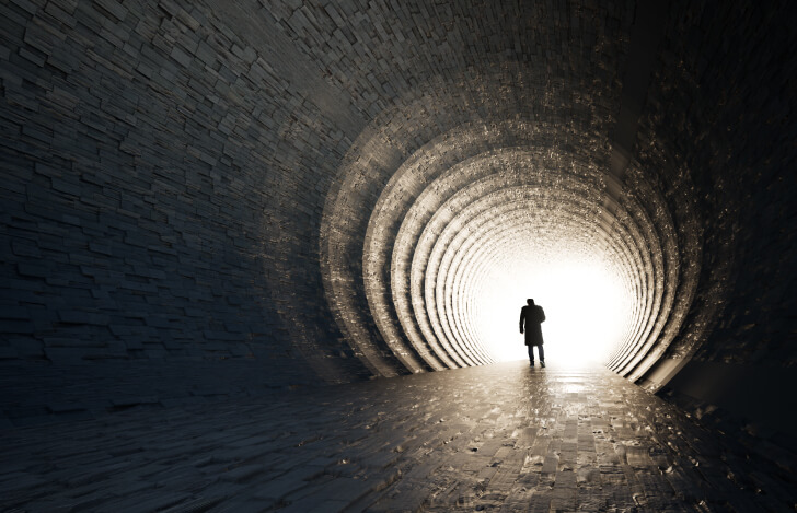 トンネルの先に見える光に向かって歩く人の姿