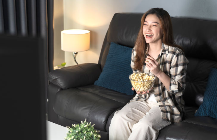 ポップコーンを手にソファでくつろぎながら映画を楽しむ女性