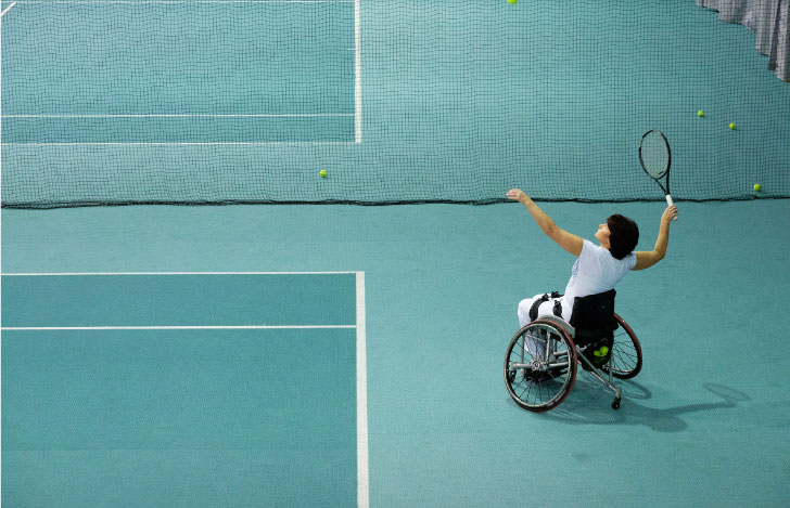 車椅子でテニスラケットを振り上げる人