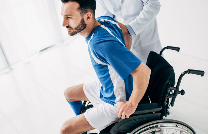 車椅子から立ち上がろうとする男性と手助けをする医師