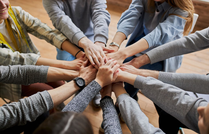 男女様々な人が腕を伸ばして手を重ねている様子