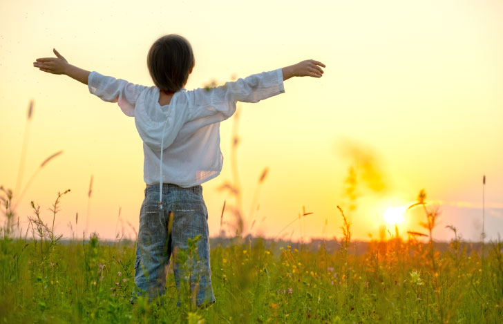夕日に向かって両手を広げる少年の後ろ姿
