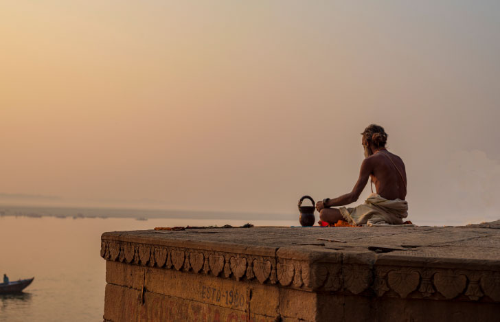 日の沈む海岸に座るインドの修行僧の背中