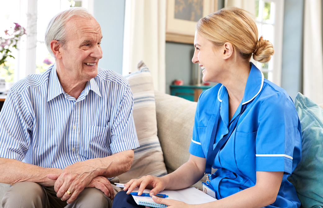 青い服を着た介護職の女性が高齢の男性と笑顔で話している