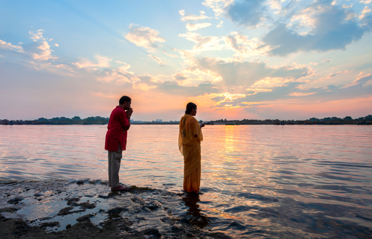 夕暮れ時の浅瀬の海で祈りを捧げるインドの男女