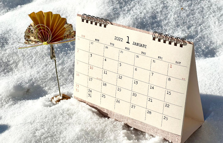 白い雪のようなものの上に置かれた卓上カレンダーと扇子のオブジェ