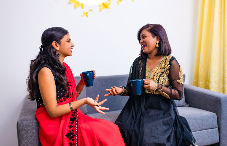 マグカップを手にソファで楽しそうに談笑する二人のインド人女性