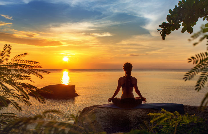 海岸で夕日に向かって瞑想する人のシルエット