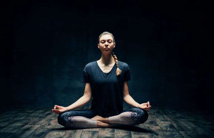暗闇の中の一筋の光の下で瞑想を行う女性