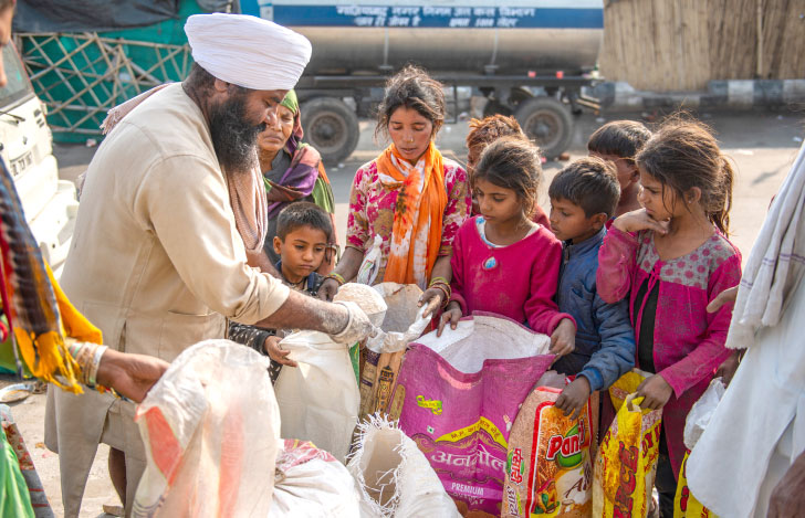 白いターバンを着たシーク教徒の男がチャリティー行為としてスラムの住む若い女の子たちに小麦粉を贈る様子