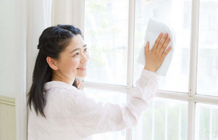 笑顔で窓を拭く白いシャツを着た女性