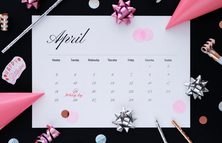 黒い台に置かれた4月のカレンダーに誕生日の印を付けるピンク色のペン