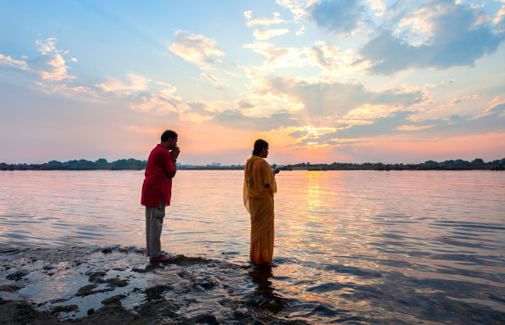夕日が沈む海の浅瀬で手を合わせて拝むインドの男女