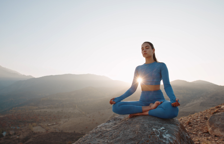丘の上で朝日を背景に瞑想する女性