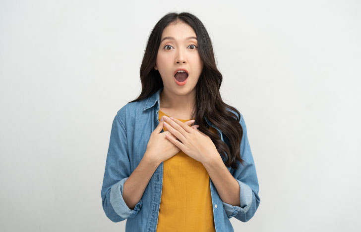 驚いた表情で両手を胸に当てるデニムシャツを着た女性