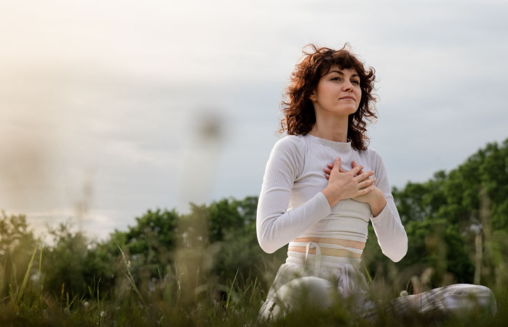 緑が茂る自然の中で胸に手をあて空を見上げる女性