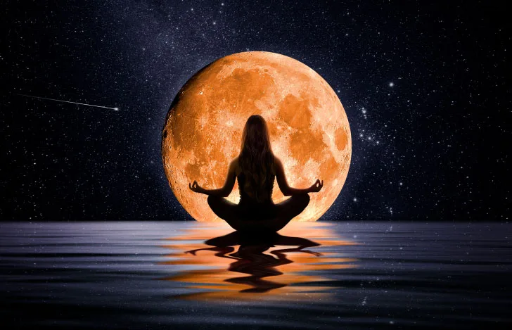 水辺に座って月に向かって瞑想する女性のシルエット