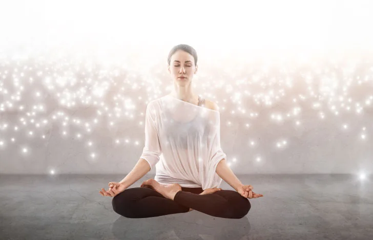 光の粒子が降り注ぐ中で瞑想する女性