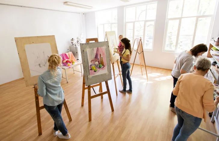 室内にイーゼルを立てて数人の女性が絵を描いている美術のクラス