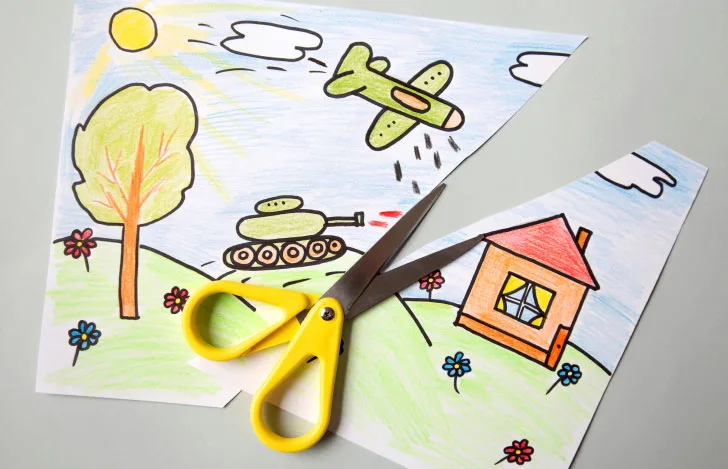 子供が描いたような家と戦争の絵をハサミで切り裂く様子