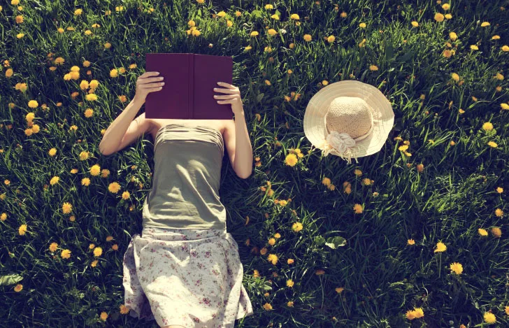 女性が草原で仰向けになって本を読む様子