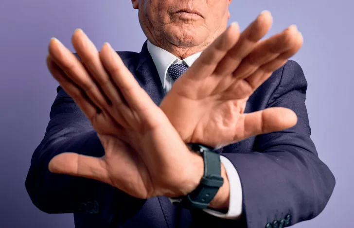 手でばつ印を作るスーツを着た初老の男性