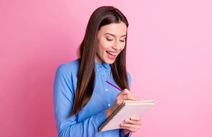 笑顔でノートに書き込む水色のシャツを着た女性