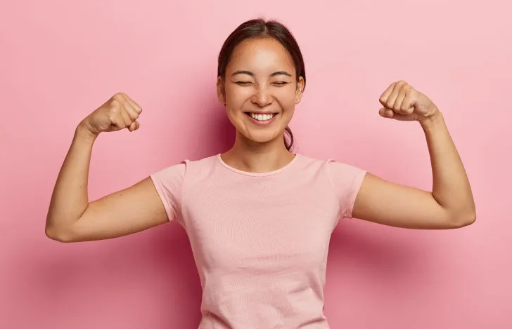 両腕で力こぶを作るピンクのTシャツを着た女性